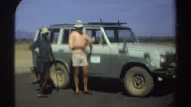 Sudan (1969): Woman Wearing Pink Shirt Leans Against Grey Car On A Sunny Day