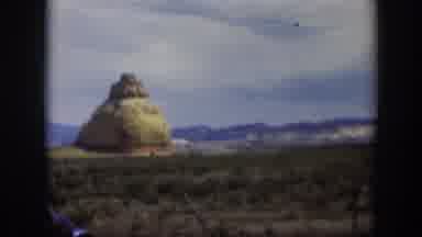 Utah (1951): View Of Black Car Parked Near Large Tan Rock On A Bright Sunny Day