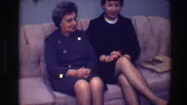 Toledo Ohio (1968): Two Women Wearing Blue And Grey Suits Sit On Tan Sofa Talking