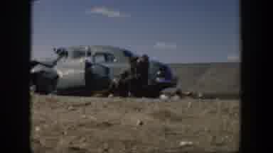 Texas (1951): Man Wearing Tan Shirt Turns To Look At Parked Black Car In A Sunny