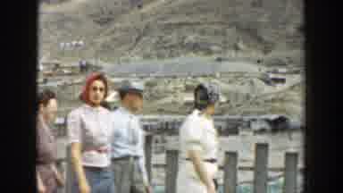 California-1937: Four People Walk Past Grey Wooden Fence On A Clear Day