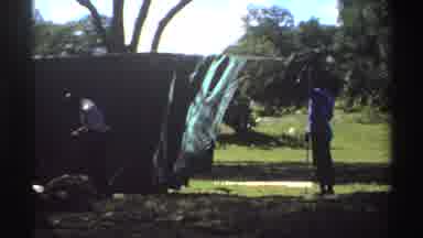 Nigeria (1969): Person Wearing White Shirt Ties Thin Tan Rope For Green Tent On A