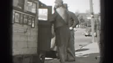 California-1939: Man Picking Up Dog While Three Men Watch on Street Corner