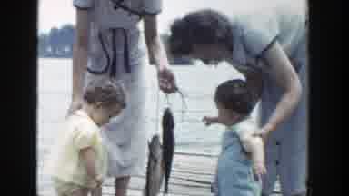 Wisconsin (1953): Woman Wearing Grey Dress Helps Baby Wearing Blue Overalls To