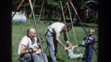 Wisconsin (1953): Two Mature Men Dressed In T-Shirts Push Babies On Swings On A