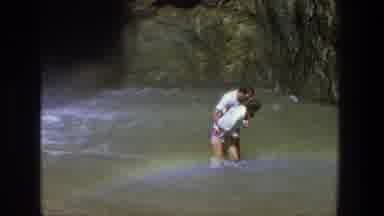 Utah (1969): Man Picking Up Woman In Water Near Cave During Windy Day