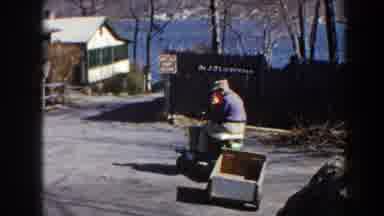 Pequot Lakes Minnesota (1964): Man Teaching Child To Drive Cargo Cart With Houses