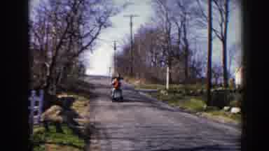 Pequot Lakes Minnesota (1964): Person Wearing Red Sweater Rides Scooter Down Road
