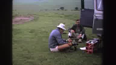 South Africa (1969): Men Sitting On The Grass Talking And Fiddling With A Camera