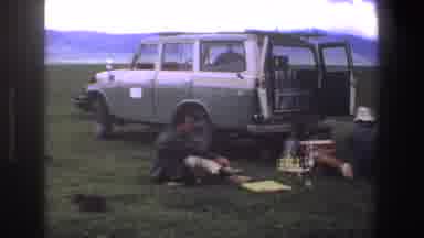 South Africa (1969): Couple Sitting on Green Grass Near Grey Truck On A Cloudy Day