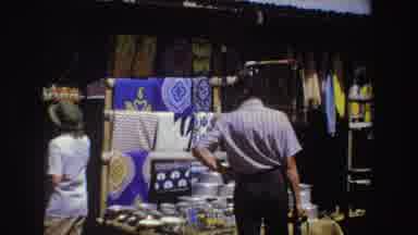 South Africa (1969): Man Wearing Grey Pants Looks At Items Displayed At Outdoor