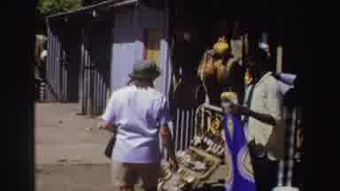 South Africa (1969): Person Wearing Blue Shirt Looks At Items On Display At