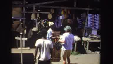 South Africa (1969): Woman In Outdoor Market Looks At Textiles And Scene Of Two