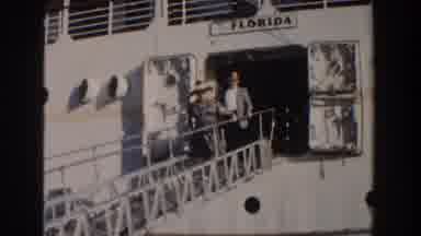 Nassau Bahamas (1961): Man Wearing Grey Jacket Waves At Camera With Hat On A Sunny