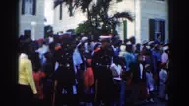 Nassau Bahamas (1961): Large Crowd Stands Near White Building And Tree On A Clear