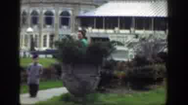 Cincinnatti Ohio (1949): Girl Wearing Yellow Coat Stands Near Green Bushes On A