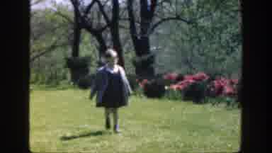 Cincinnatti Ohio (1949): Child Wearing Gray Coat Walks Past Blooming Red Flowers