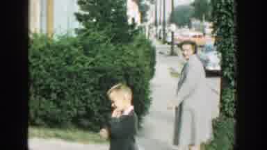 Wisconsin (1964): Woman Wearing Light Gray Coat Walks With Small Boy Wearing Black