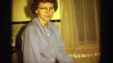 Wisconsin (1964): Woman Wearing Blue Shirt And Glasses Nods At Camera While Man
