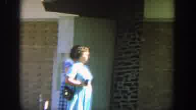 Wisconsin (1964): Two Women Walk Past Tan Brick Building On A Sunny Day