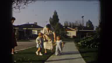 California (1958): Woman Wearing Yellow Dress Picks Up Toddler Wearing Blue