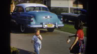 California (1958): Male Toddler In Denim Overalls Running Outside Towards Young