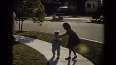 California (1958): Girl Wearing Red Dress Gives Object To Toddler Wearing Blue