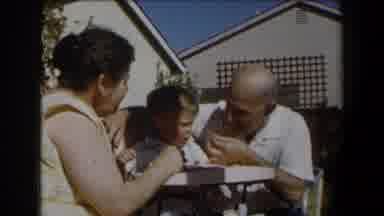 California (1958): Man Wearing White Shirt Tries Feeding Baby Sitting In White