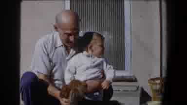 California (1958): Older Man Sitting On A Stoop With A Dog Trying To Get A Young