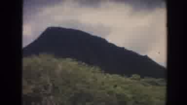 Hawaii (1961): A Sharp Rocky Peak Above Dense Trees With Sky In The Background