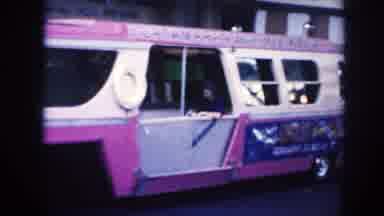 Hawaii (1961): Woman Wearing Black Dress Waves From Red Bus On A Clear Day
