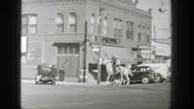 Wyoming (1939): Two Men Ride Galloping Horses Through Town Past A Row Of Cars