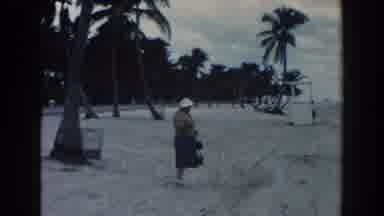 Miami Florida (1960): Woman Wearing Blue Skirt Picks Up Object From Sand On A