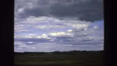 Sweden (1975): Driving On The Road Passing By Green Grassy Field Under Cloudy Sky
