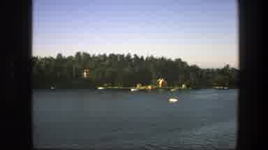 Sweden (1975): A Single Boat Floats In A Lake With Various Buildings And Trees