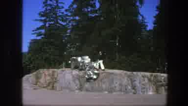 Sweden (1975): Person Wearing White Pants Walks Past Silver Sculpture On A Sunny