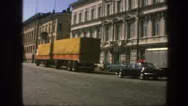 Sweden (1975): View Of Yellow Truck And Tan Tour Bus Driving Uphill Past White