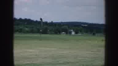 Nebraska (1958): White Airplane Lands In Large Green Field On Clear Day