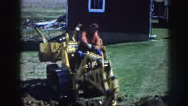 Nebraska (1958): Man Wearing Red Shirt Operates Yellow Backhoe On A Sunny Day