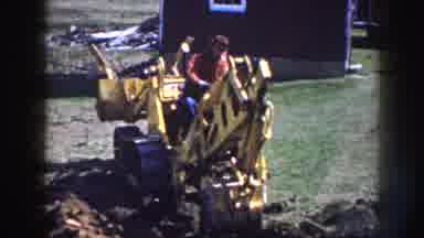 Nebraska (1958): Man Wearing Red Shirt Sits On Yellow Backhoe On A Sunny Day