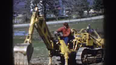 Nebraska (1958): Old Man Maneuvering Small Excavator To Dig Hole In Open Field