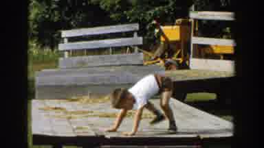 Michigan (1958): Boy Wearing Brown Shorts Stands Up On Wooden Platform On A Sunny