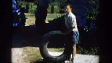 Michigan (1958): Boy Wearing Blue Shorts Holds Black Tire On A Bright Sunny Day