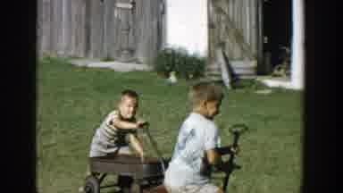 Michigan (1958): Two Children Pull Wagons On Lawn In Front Of A Fence And Shed