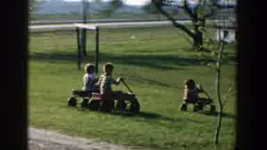 Michigan (1958): Three Children Riding Toy Motor Bikes On The Lawn As One Falls