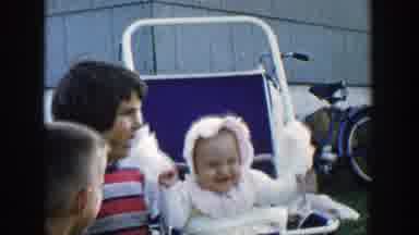 Michigan (1958): Baby Wearing White Hat Flaps Arms While Sitting In Blue Stiller