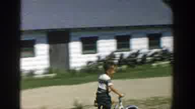 Michigan (1958): Boy Wearing Black Shorts Rides Bicycle On A Bright Sunny Day