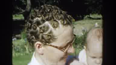 Michigan (1958): Woman Wearing Glasses Holds Baby Wearing White Shirt On A Sunny
