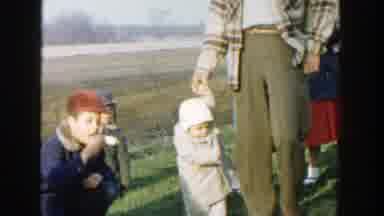Michigan (1958): Man Wearing Brown Pants Holds Hand Of Toddler Wearing White Hat