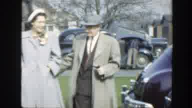 Massachusetts (1949): Man Wearing Gray Coat Walks To White Garage Doors On A Clear